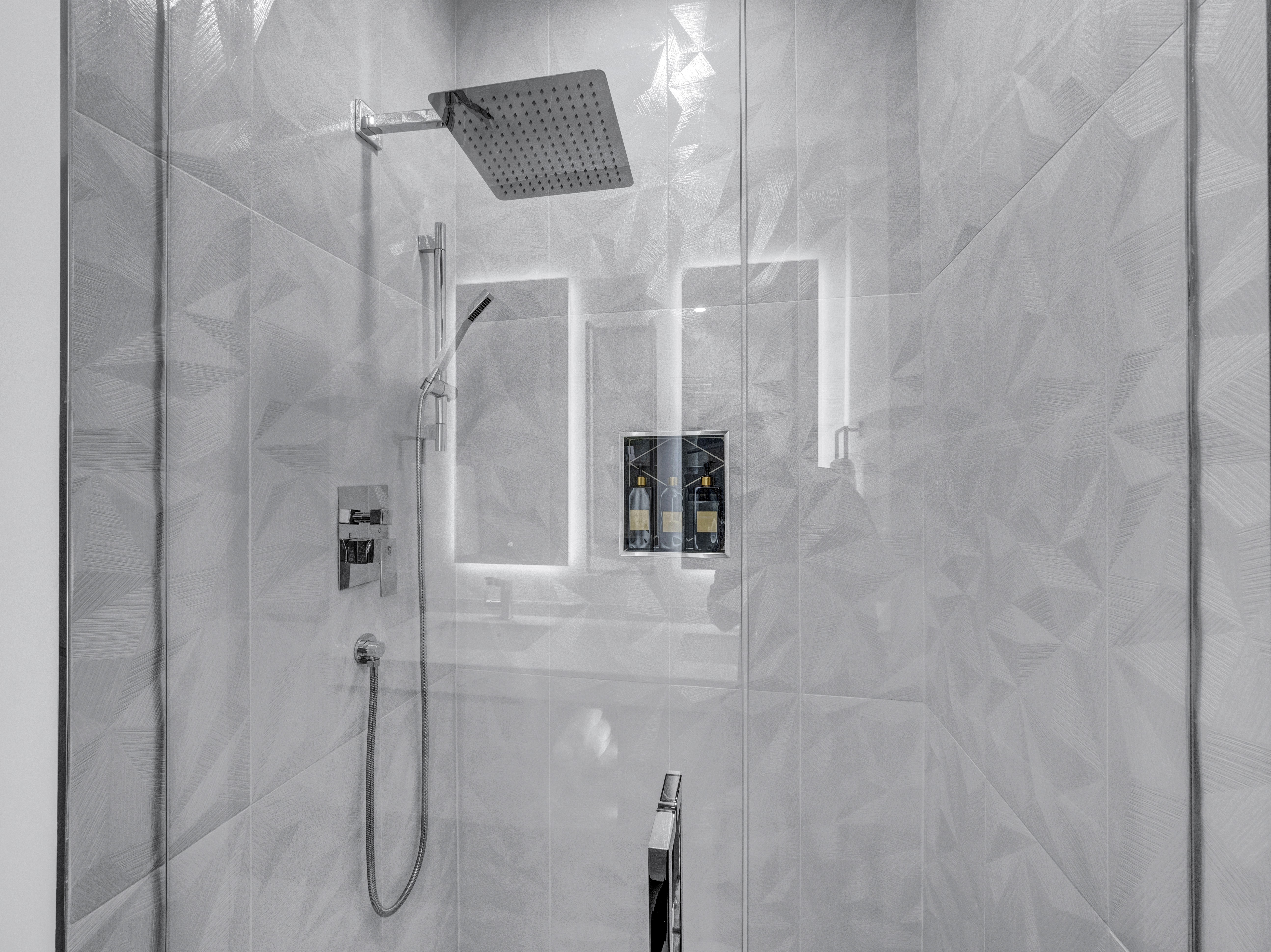Close-up of a glass walk-in shower featuring textured geometric tiles and a modern square rainfall showerhead