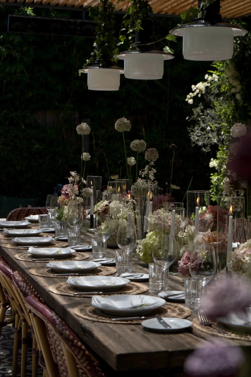 Perspectiva de mesa exterior con centros de mesa de hortensias, rosas y flores de tallo largo en ambiente relajado.