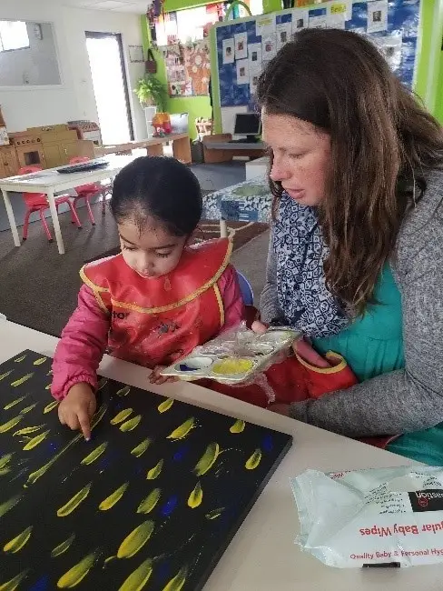 Educator assisting a student with finger painting.