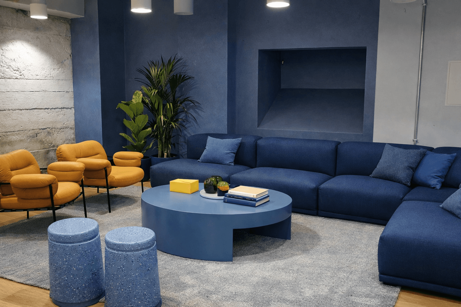 Modern interior space with a blue circular coffee table, flowers in a vase, and books neatly arranged.