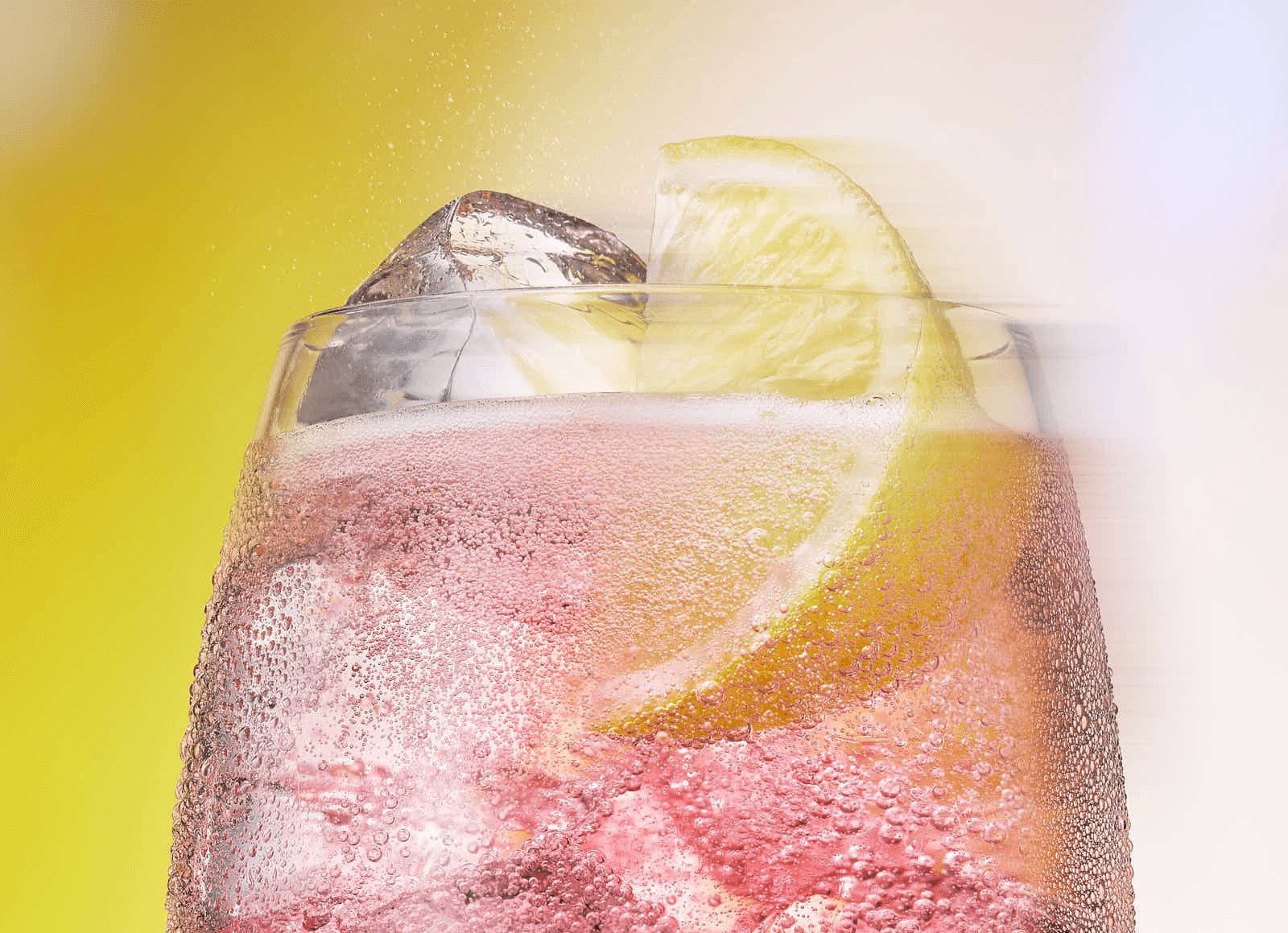 A close-up of a refreshing pink beverage with ice and a slice of lemon on the rim, against a bright background.