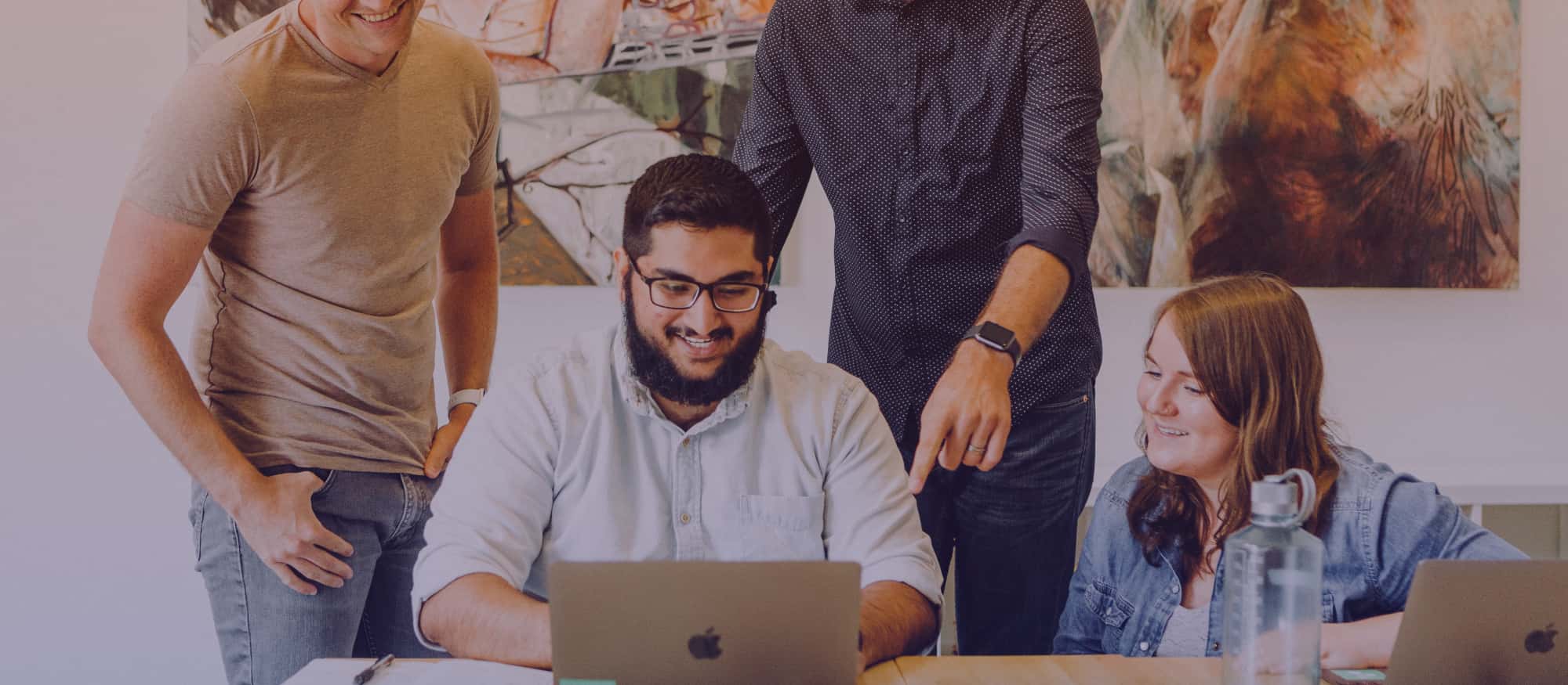 A group of colleagues around their coworkers working on the laptop.