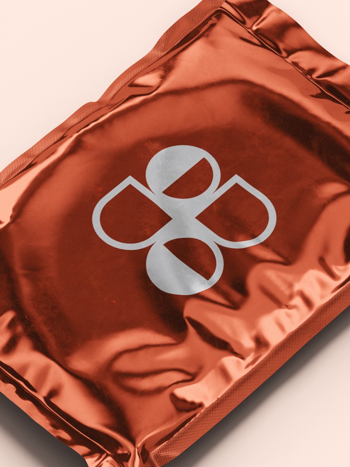 Metallic red-orange foil pouch with a reflective silver ODE logo printed at its centre, photographed on a pale peach background.