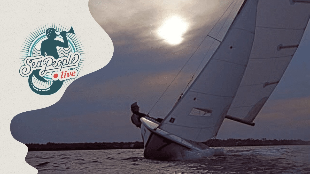 Conor Dugan sails a small sailboat heeled over on the water beneath full sails as the sun breaks through the clouds.