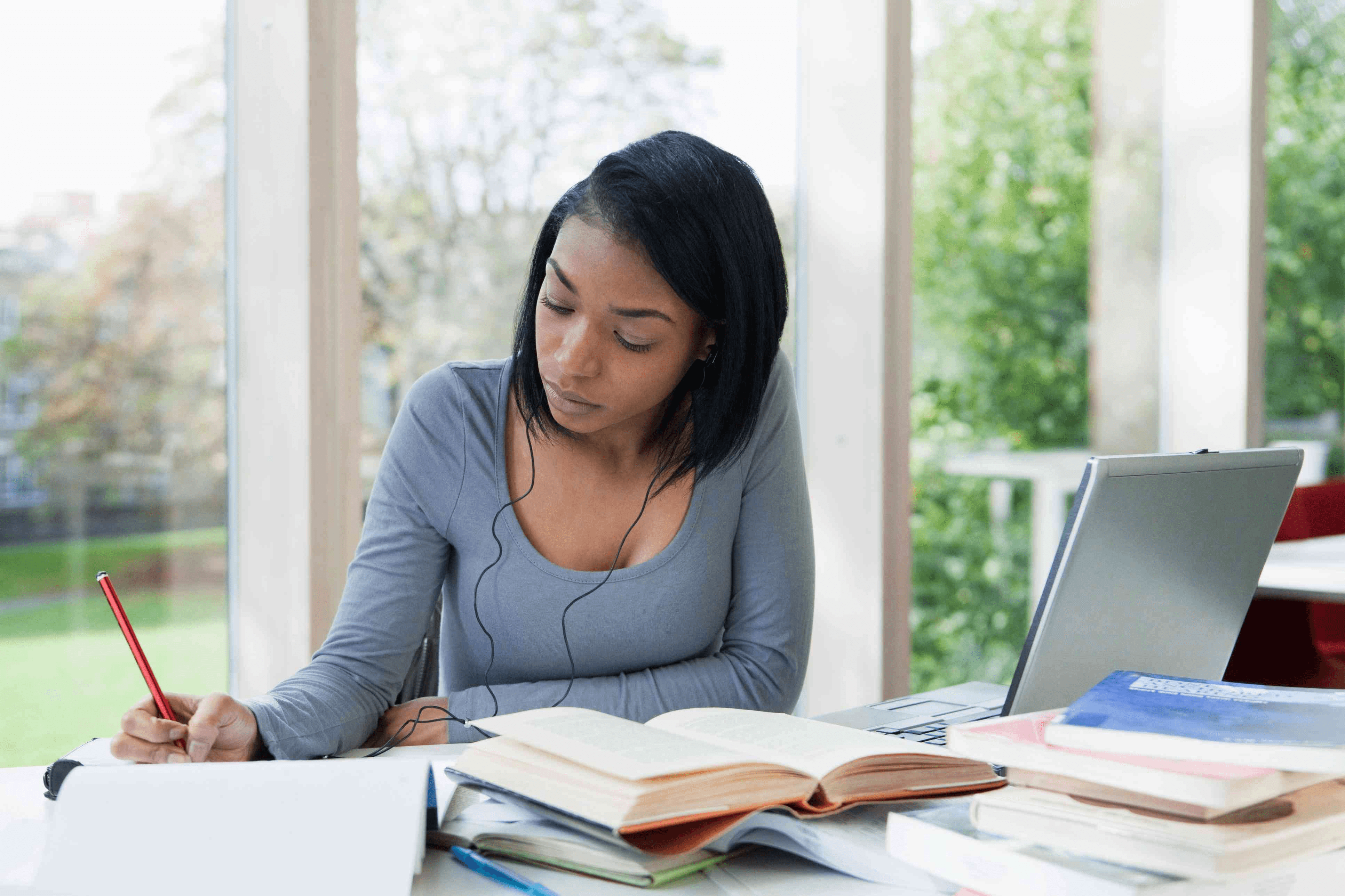 A high school student balancing part-time work and academic research at a desk with textbooks, notes, and a laptop