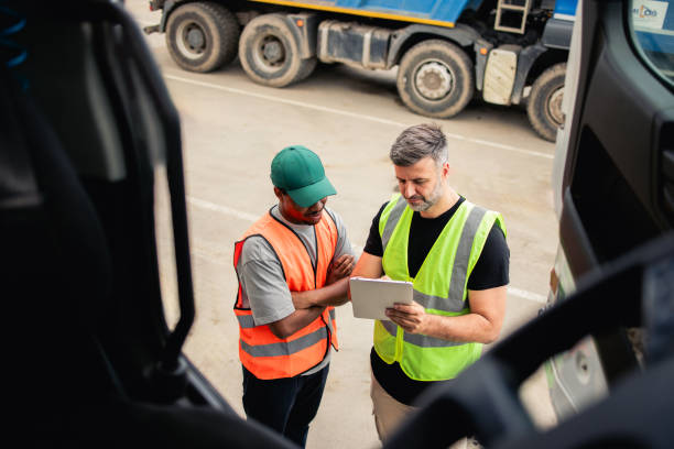 image taken from insde the cab of a lorry and outside is two men checking a document wearing high vis