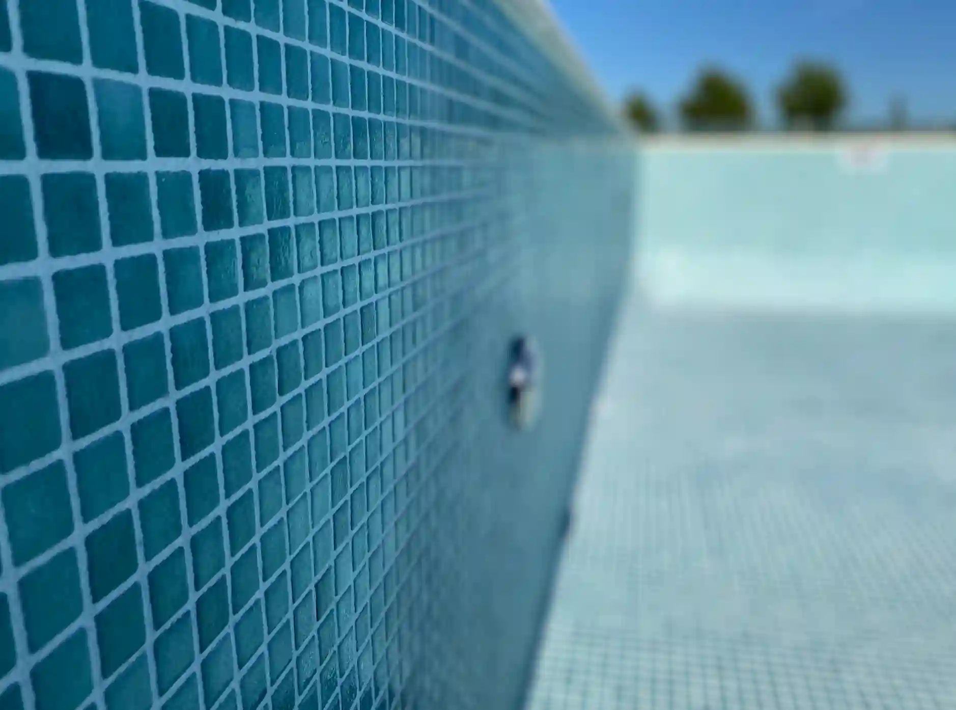 Primer plano macro de la pared de una pileta de diseño, resaltando la textura y calidad del revestimiento de venecitas turquesas.