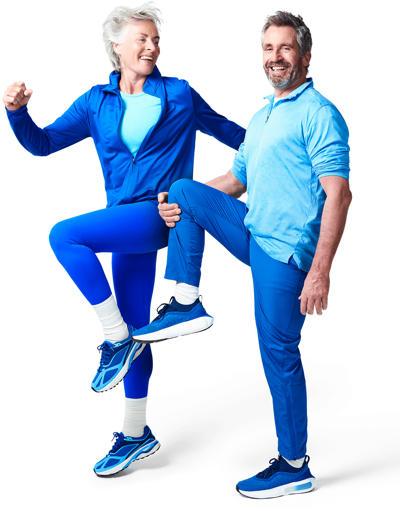 A man and woman in coordinating blue outfits, playfully lifting their legs while smiling at the camera.