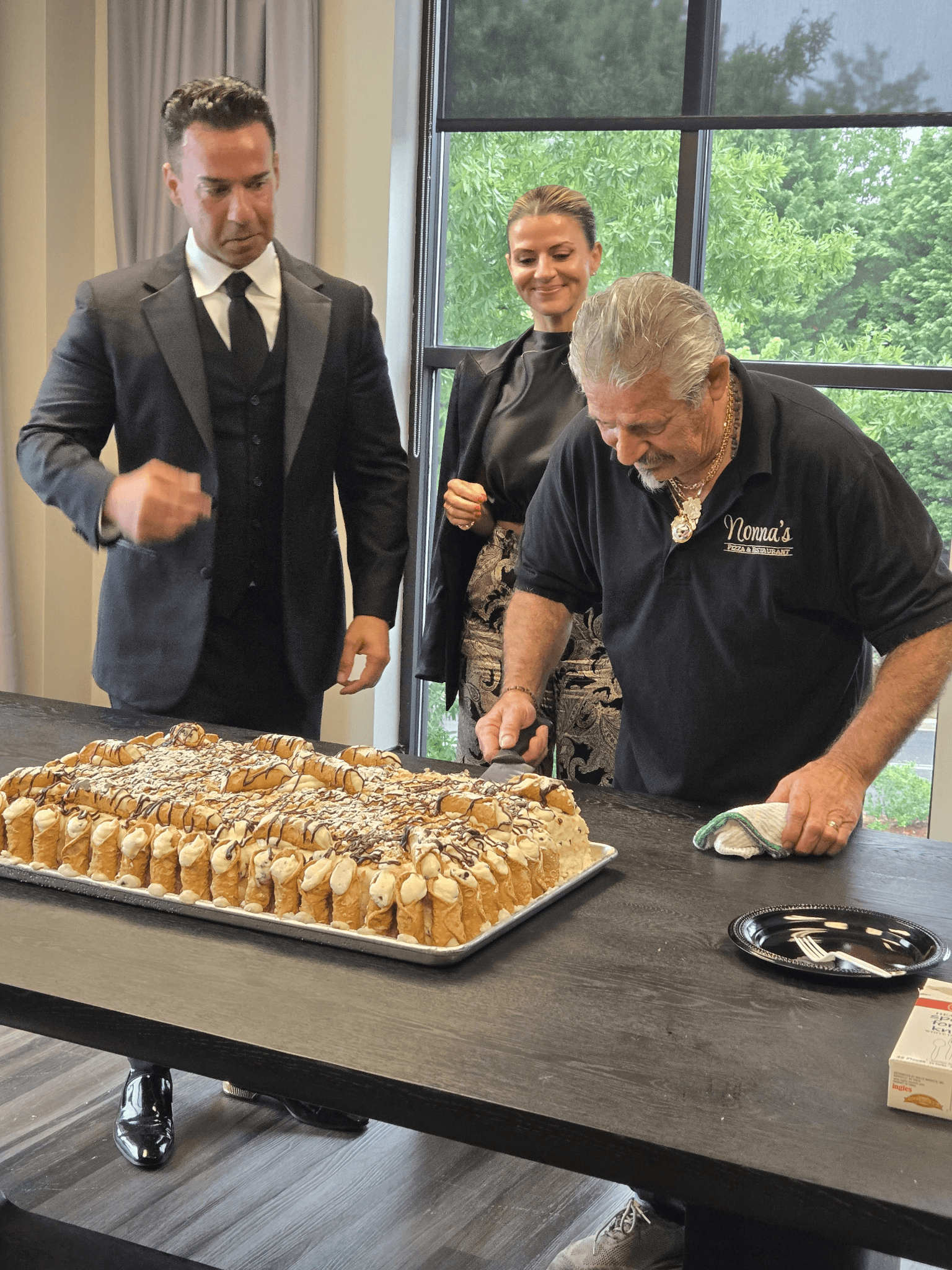 Chef Francesco cuts a large Italian dessert cake as guests watch during a celebration.