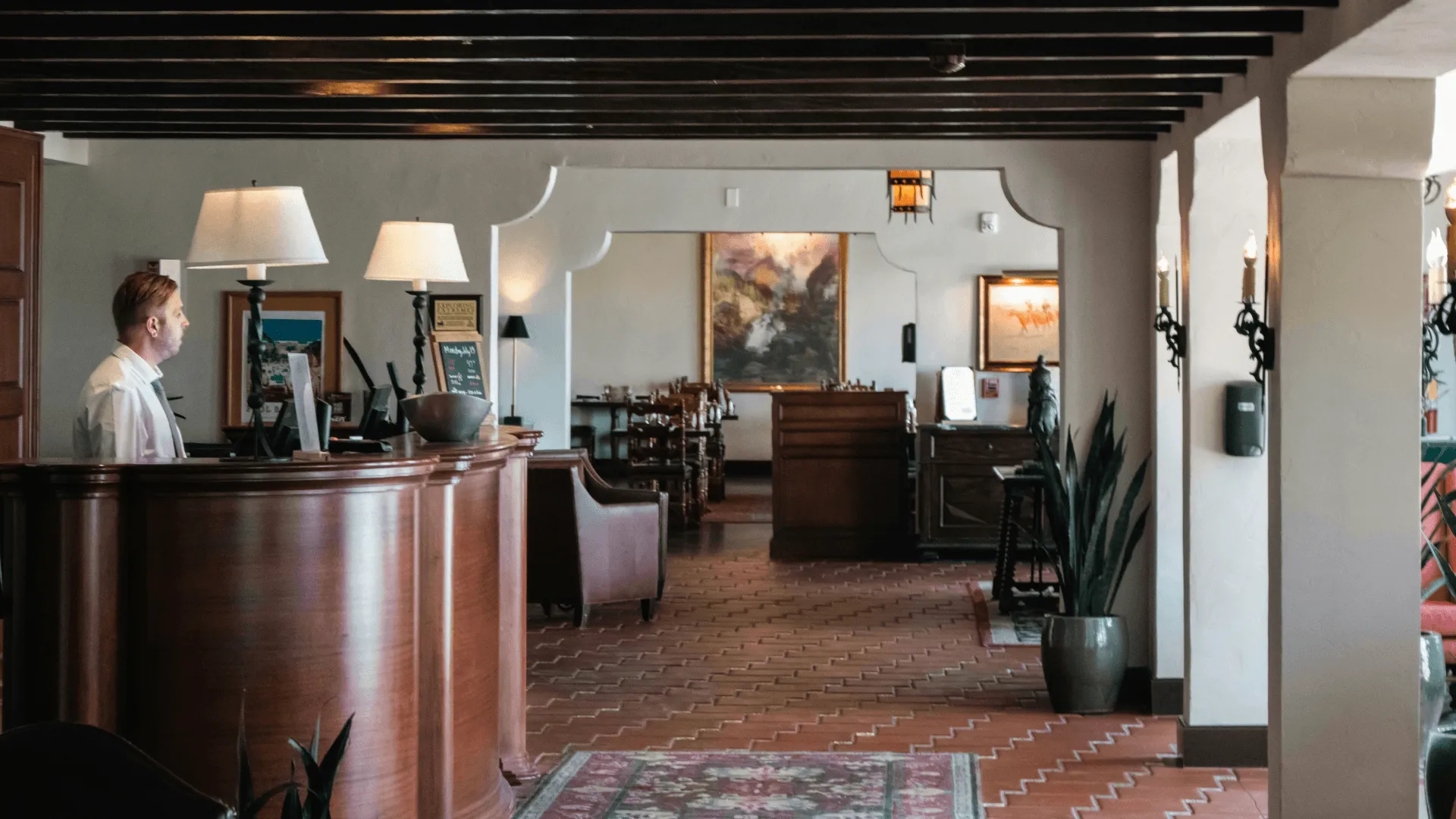 A wide shot of a hotel lobby with reception desk and person standing behind it
