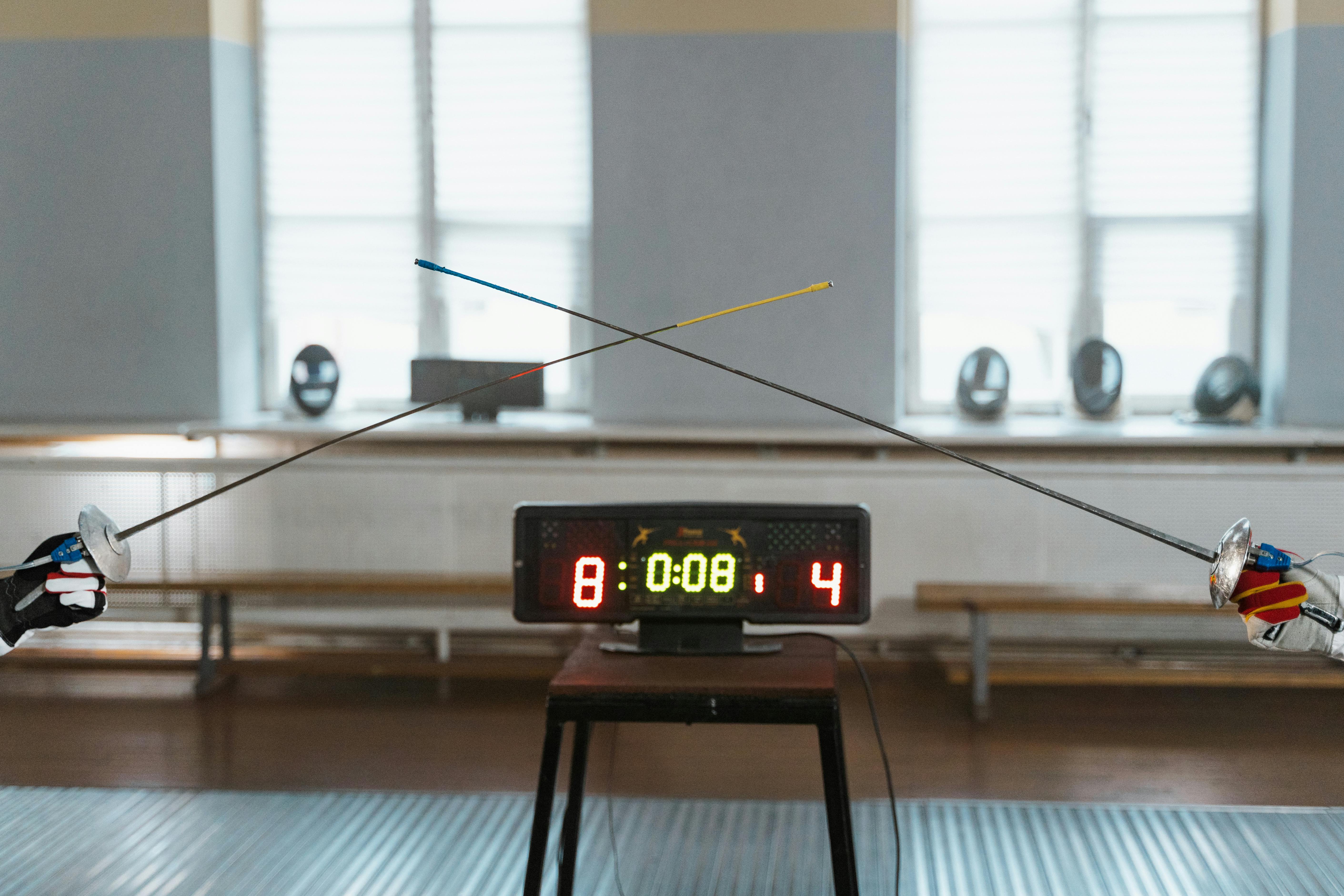Fencing bout showing the fencer’s hands, epees, and the scoreboard