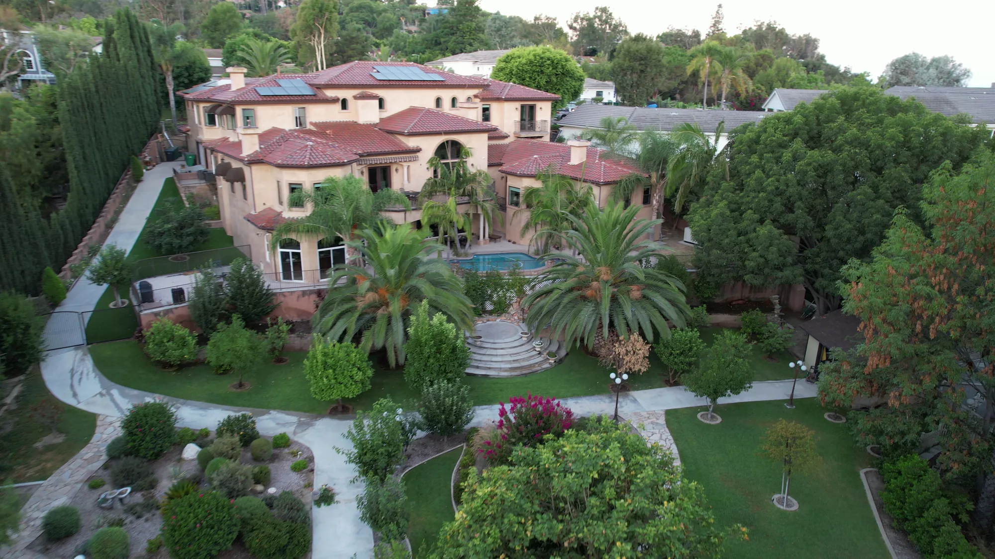 Aerial view of a home with a pool terrace, palm trees, lawn and winding garden paths.