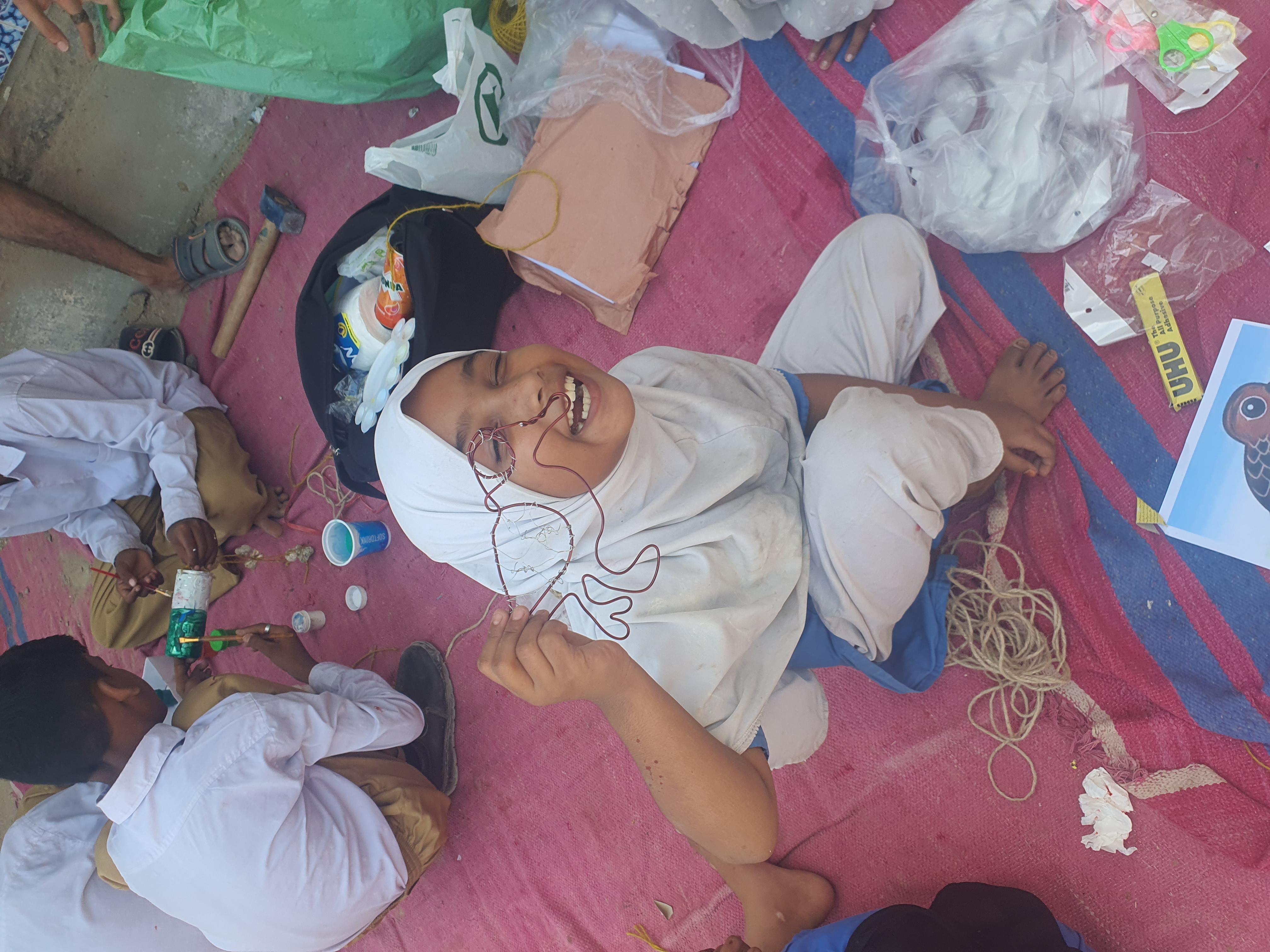 A smiling young child in Hijab holding up her artwork, during a training during CFAW's Mangroves Project