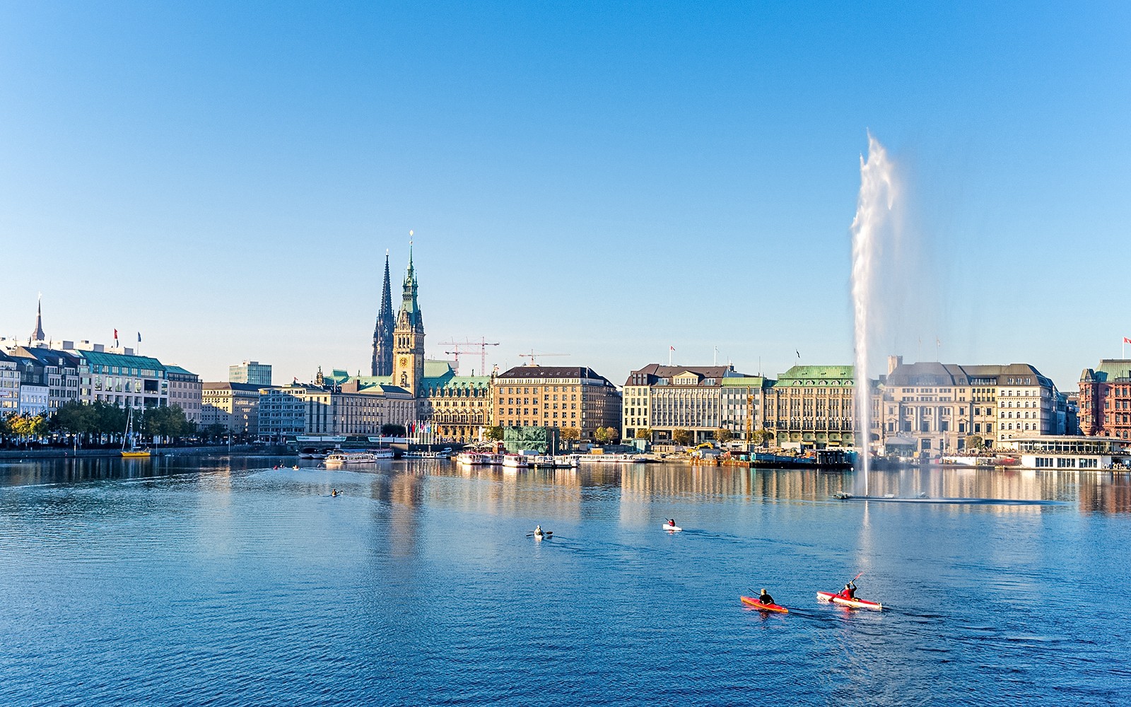 Hamburg cityscape with kayakers on Alster Lake and St. Nicholas' Church in view.