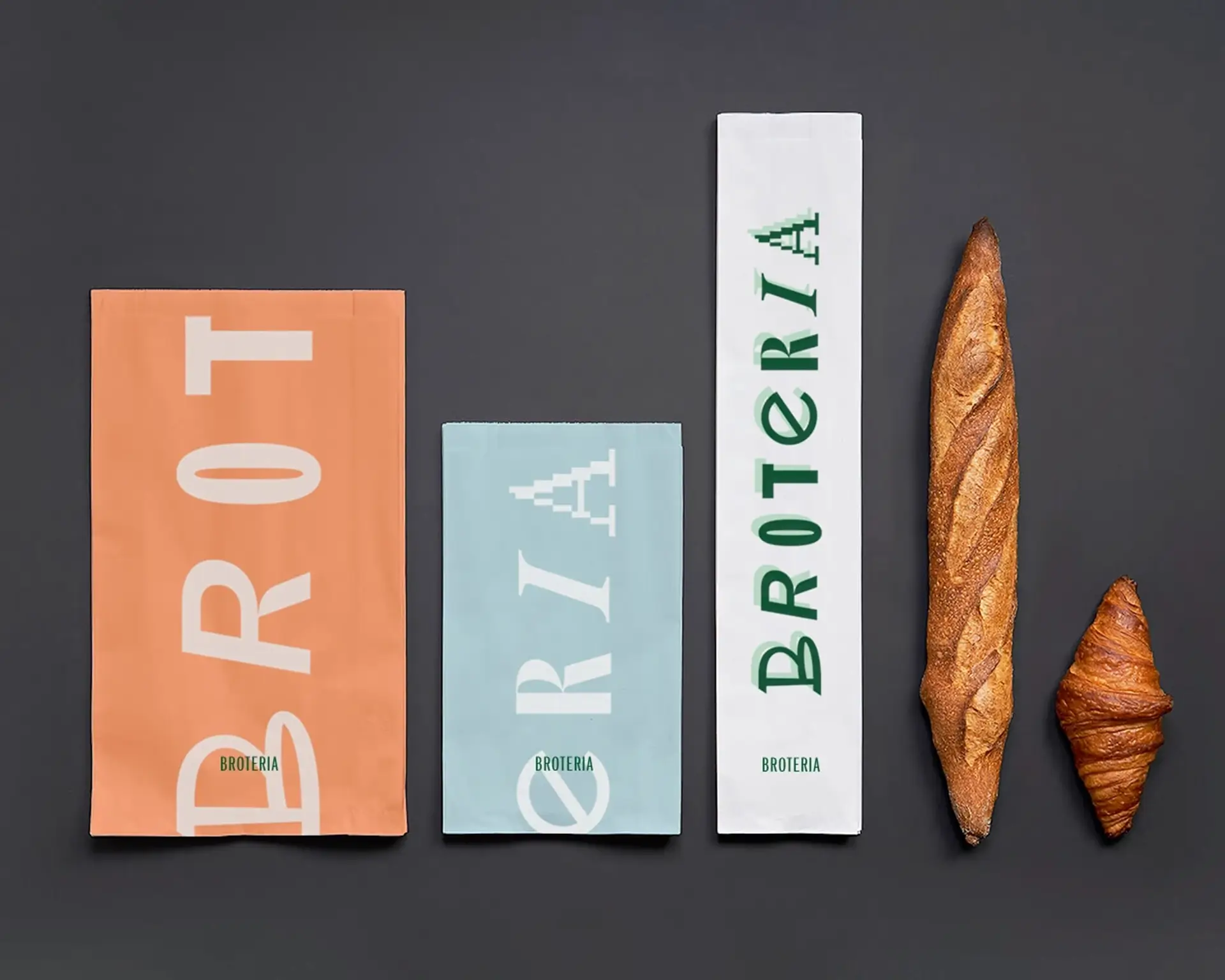 Broteria paper bread bags in peach, blue, and white beside baguette and croissant