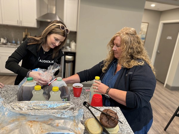 A woman in a red top sits at a desk, talking to someone out of view in an office setting.
