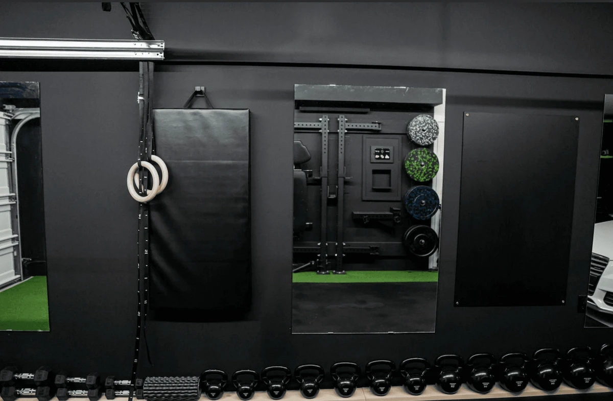 Calgary garage home gym with wall-mounted storage, gymnastic rings, weight plates, and turf flooring designed for versatile functional training