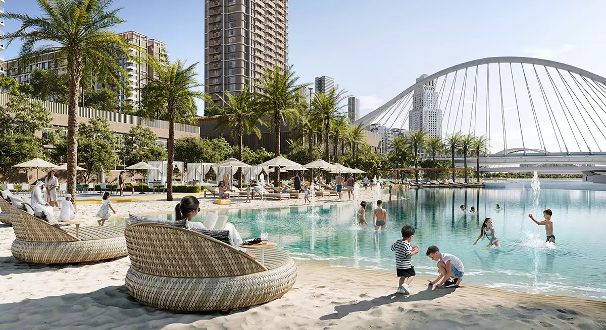 Beach-inspired swimming pool at Aeon Dubai featuring palm trees, sunbeds, and children playing near the waterfront with a modern bridge in view.