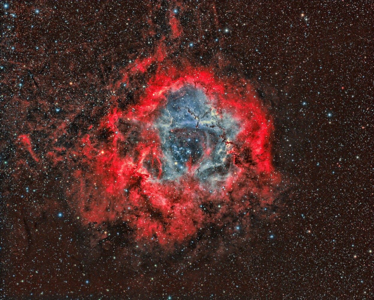A vibrant, colorful nebula with a blue core surrounded by red gas and dust against a starry background.