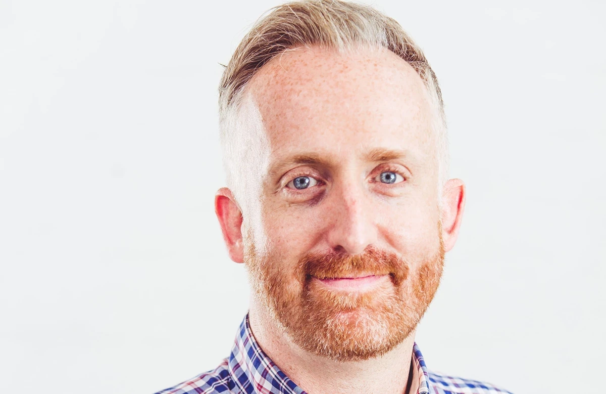 A person wearing a checked shirt is shown from the shoulders up against a plain white background.