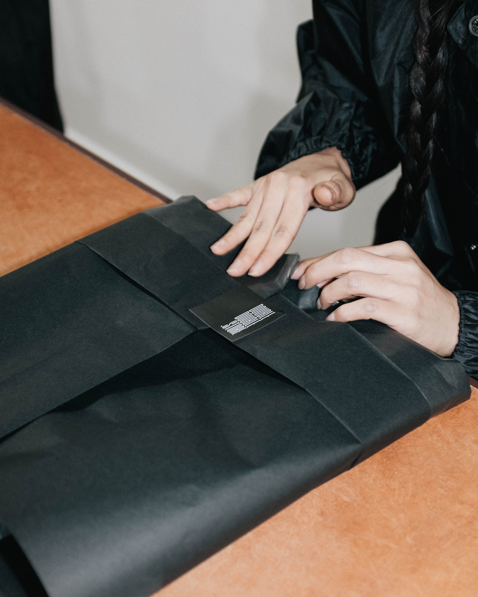 Close-up of in-store packaging at Double Double, with folded garment wrapped in black paper on a timber counter.