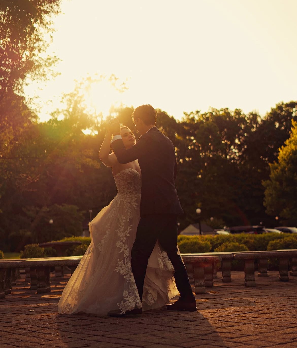 A couple in wedding attire walks hand in hand across a sunlit field.
