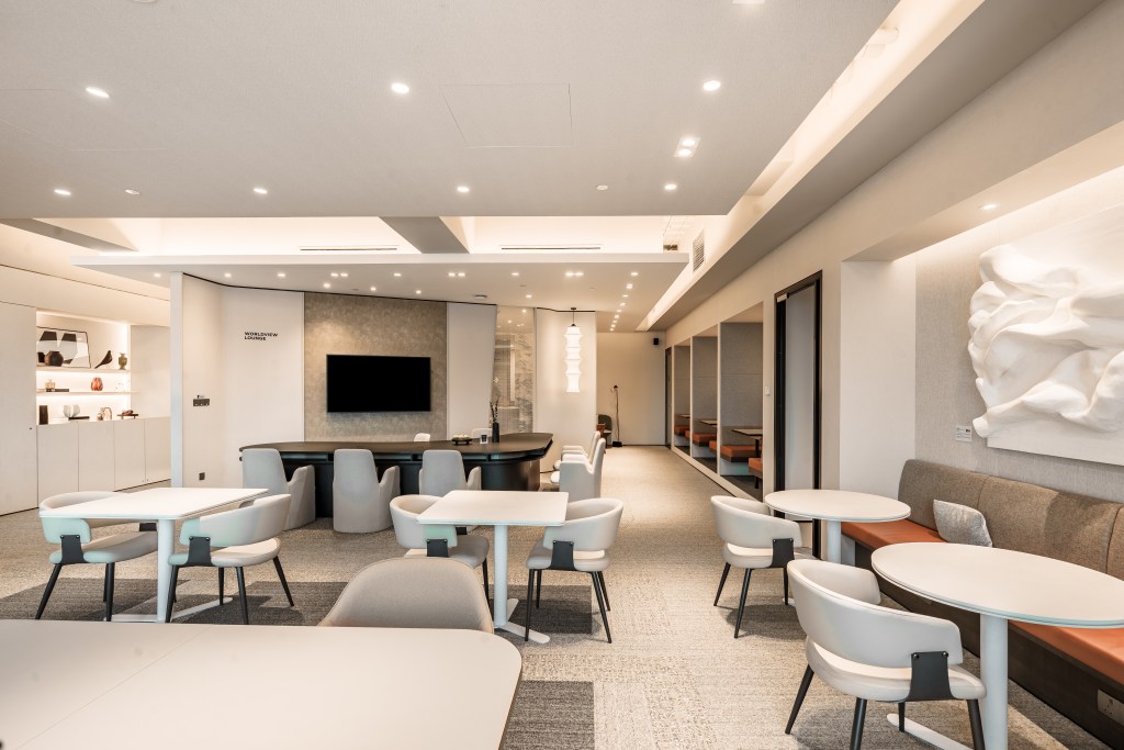 Modern coworking space with stylish furniture and warm lighting, featuring a meeting area with a large screen and a cozy seating arrangement, creating an inviting atmosphere.