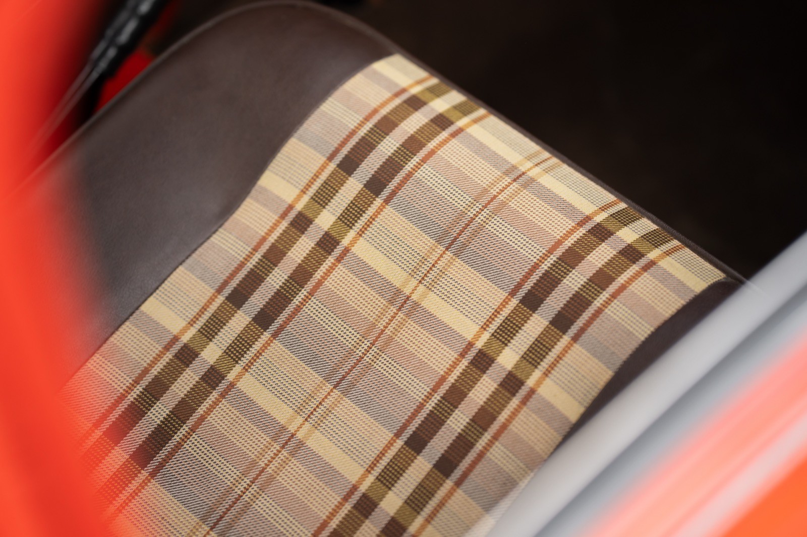 Close-up of a textured car seat with a plaid pattern, featuring shades of brown and beige, set against a bright backdrop.
