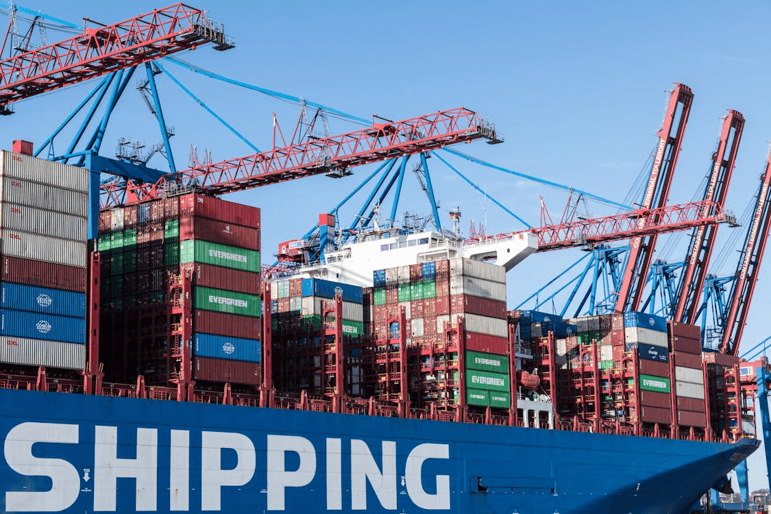 Three people in trench coats walk past a neon storefront.