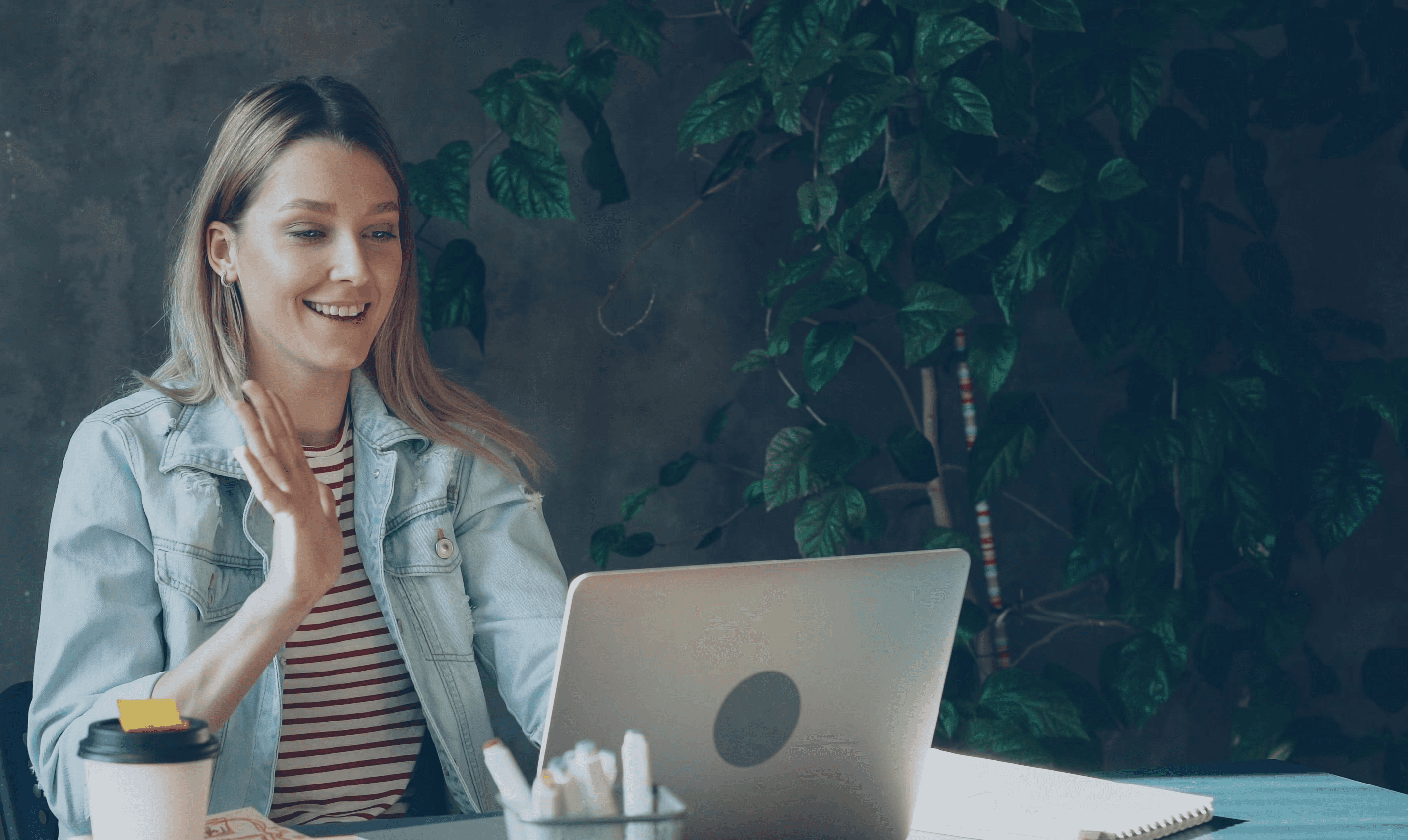 Woman waving during a video call on her laptop.