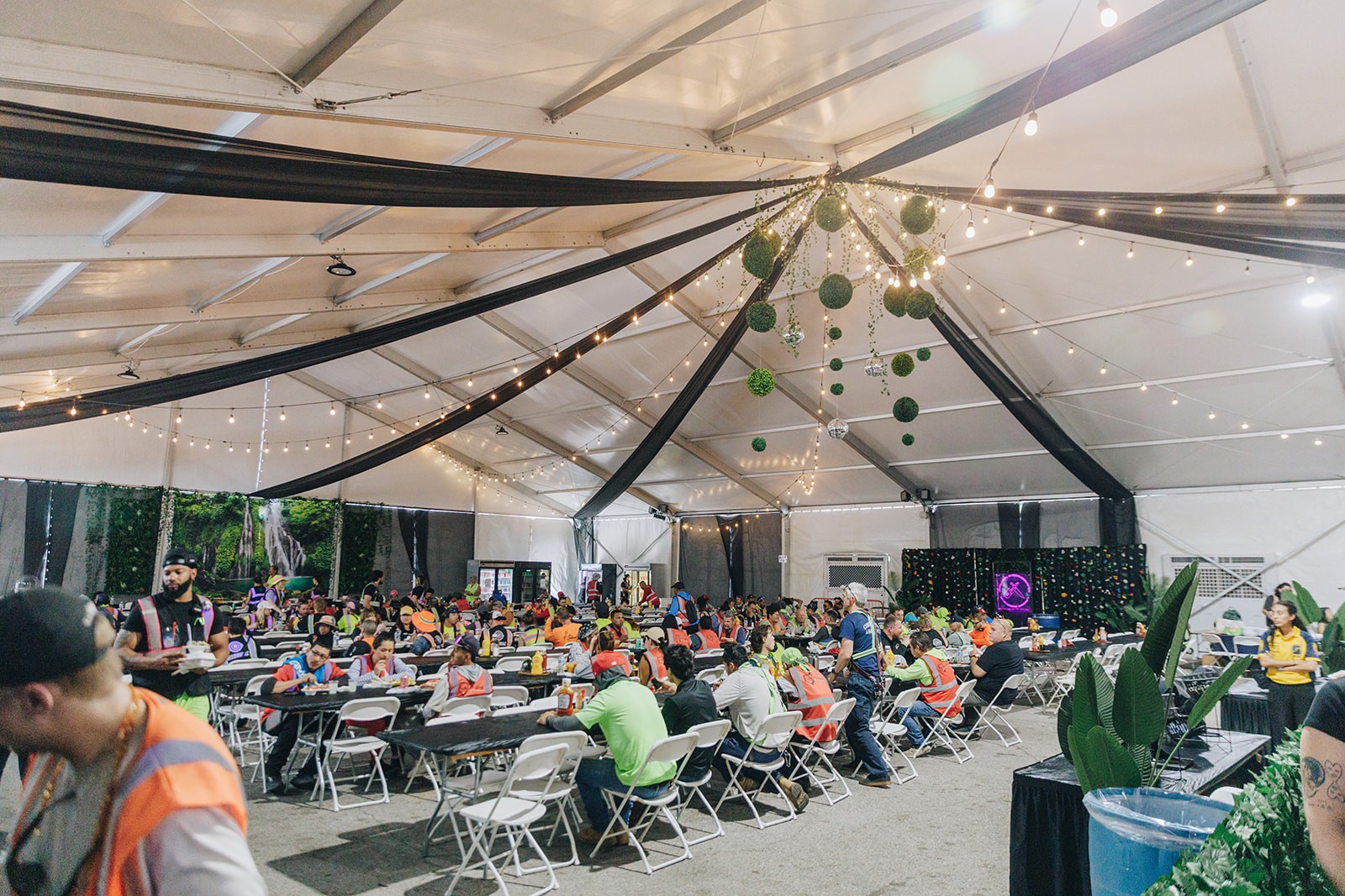 A spacious indoor setting with a high, tent-like ceiling, filled with people seated at long tables.