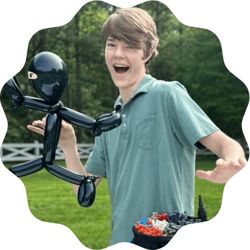 Elias smiling and posing with a black stickman balloon twist and a bucket of balloon twisting supplier