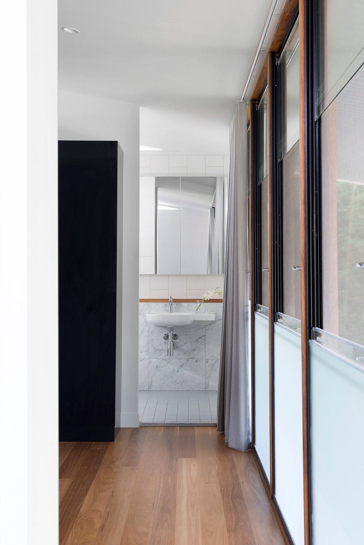 Quiet bedroom with restrained palette, timber bedside joinery, and soft natural light against white walls.