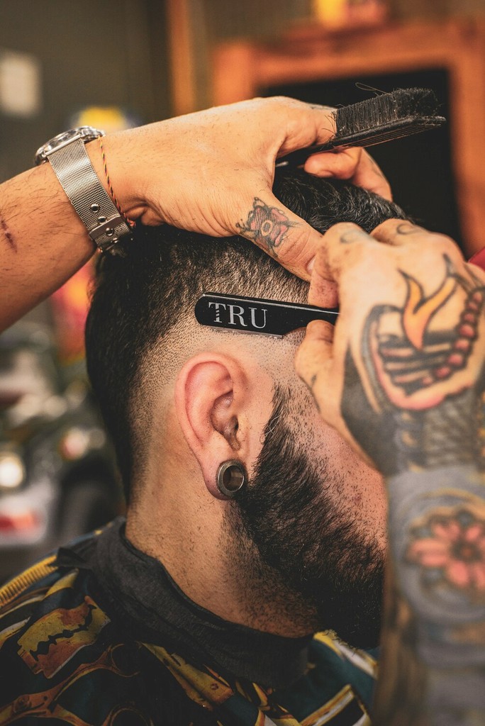 Barber Styling a Beard: A skilled barber meticulously shaping and trimming a full beard for a middle-aged male client in a modern barbershop with contemporary decor.