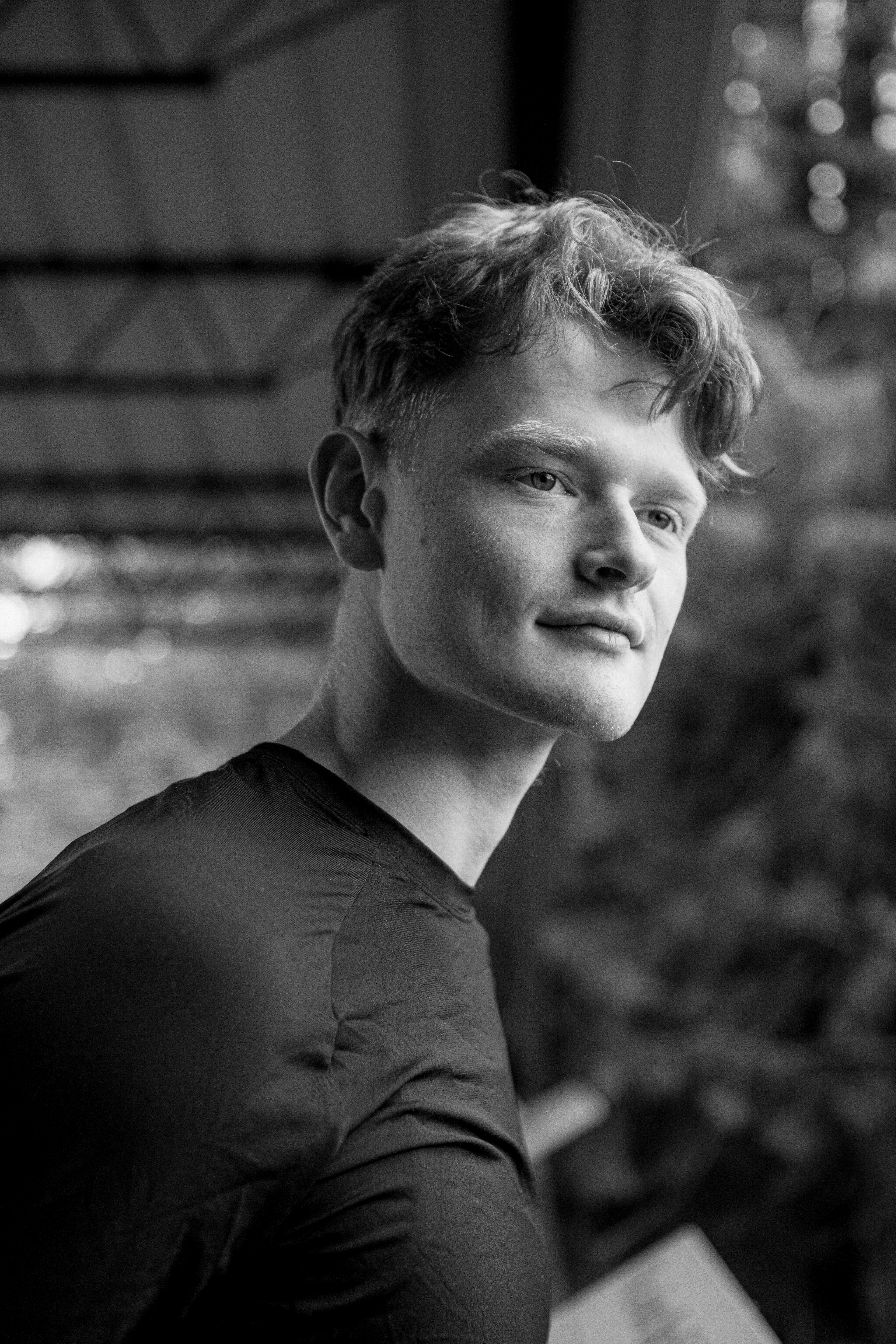Person wearing a blue puffer jacket and red backpack standing in front of a light blue building on a city street.