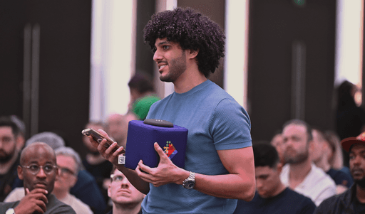 In a bustling Dubai event, a man in a blue shirt actively participates during question time by holding a microphone amidst a diverse audience.