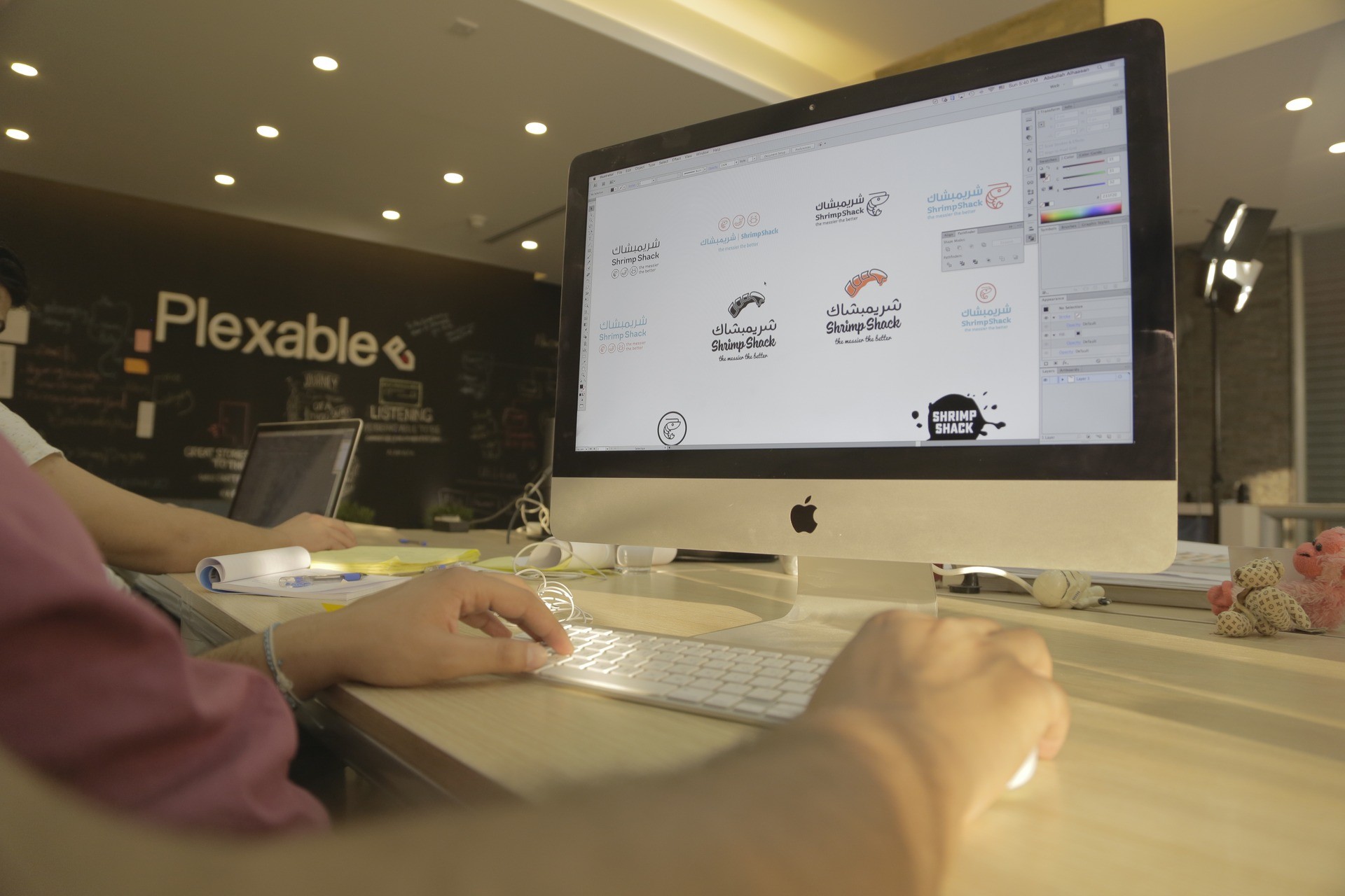 Designers reviewing bilingual logo concepts on an iMac in the Plexable studio