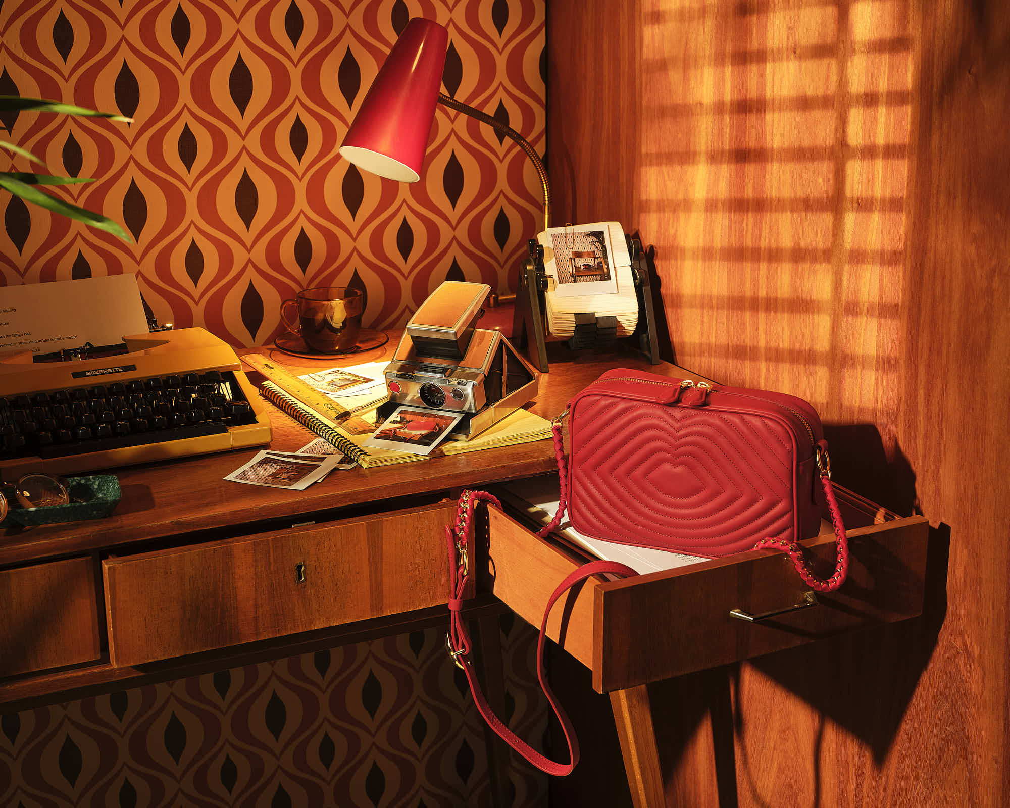 Vintage desk with typewriter and red handbag in warm retro office setting.