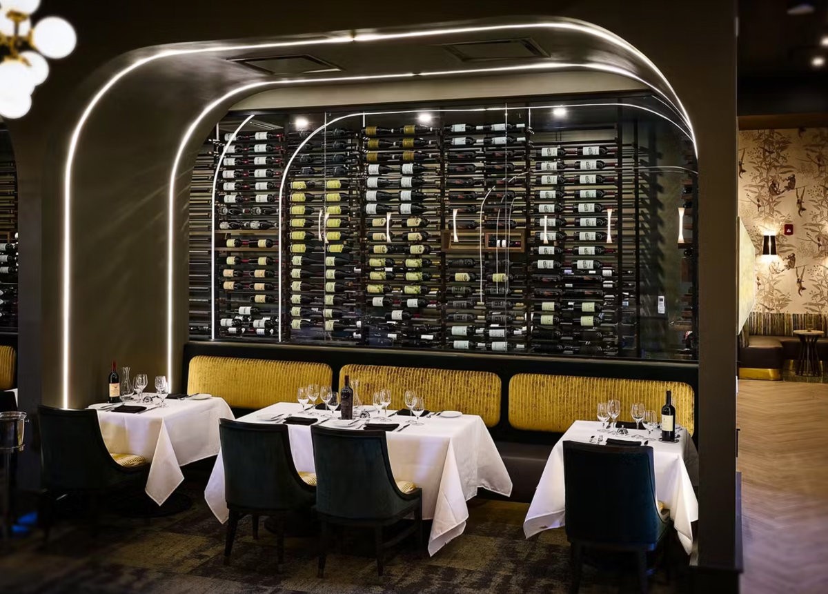 A restaurant dining area with a large wine wall behind a booth with tables set for two. 