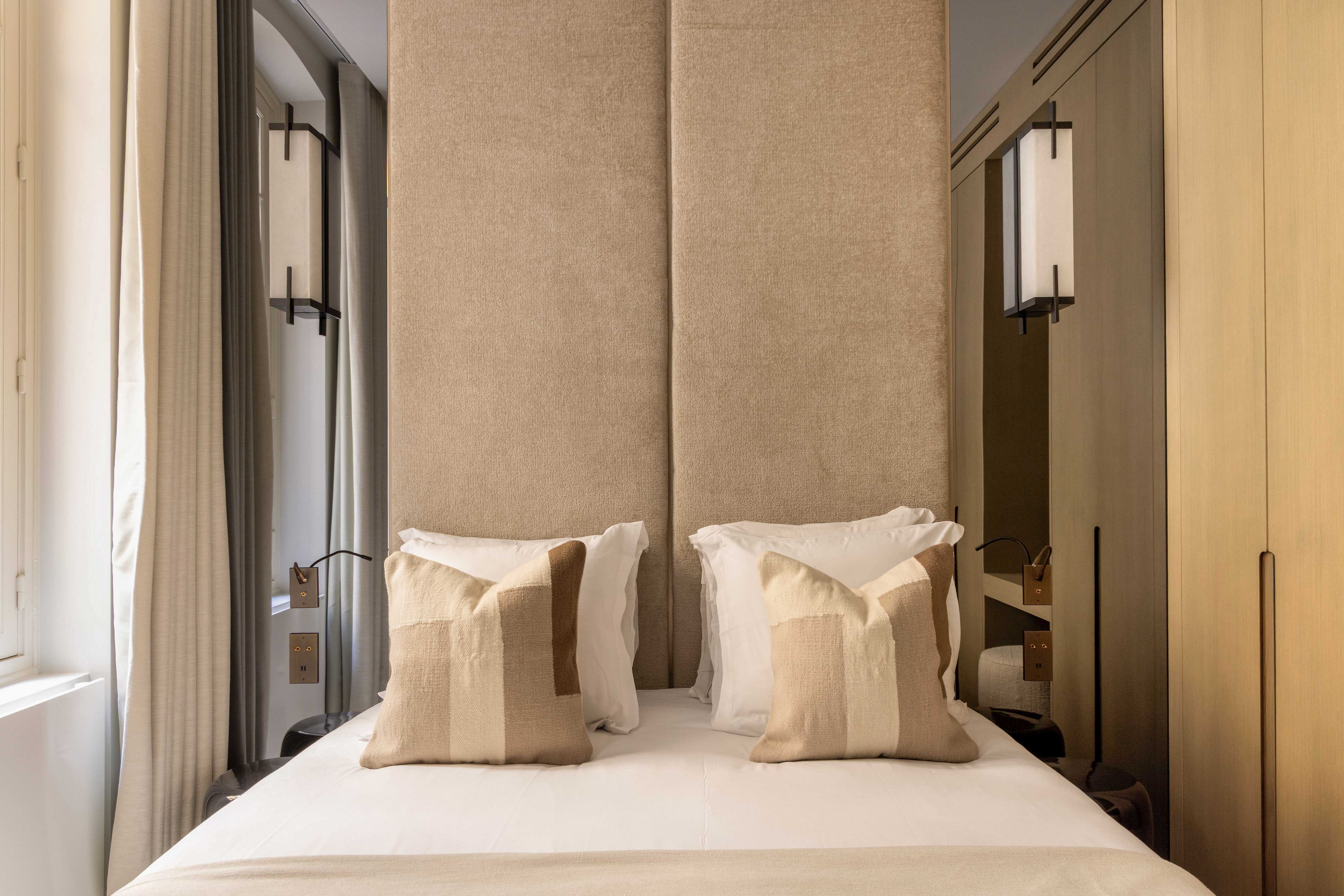 Lit double avec tête de lit haute en velours beige, coussins assortis et appliques murales