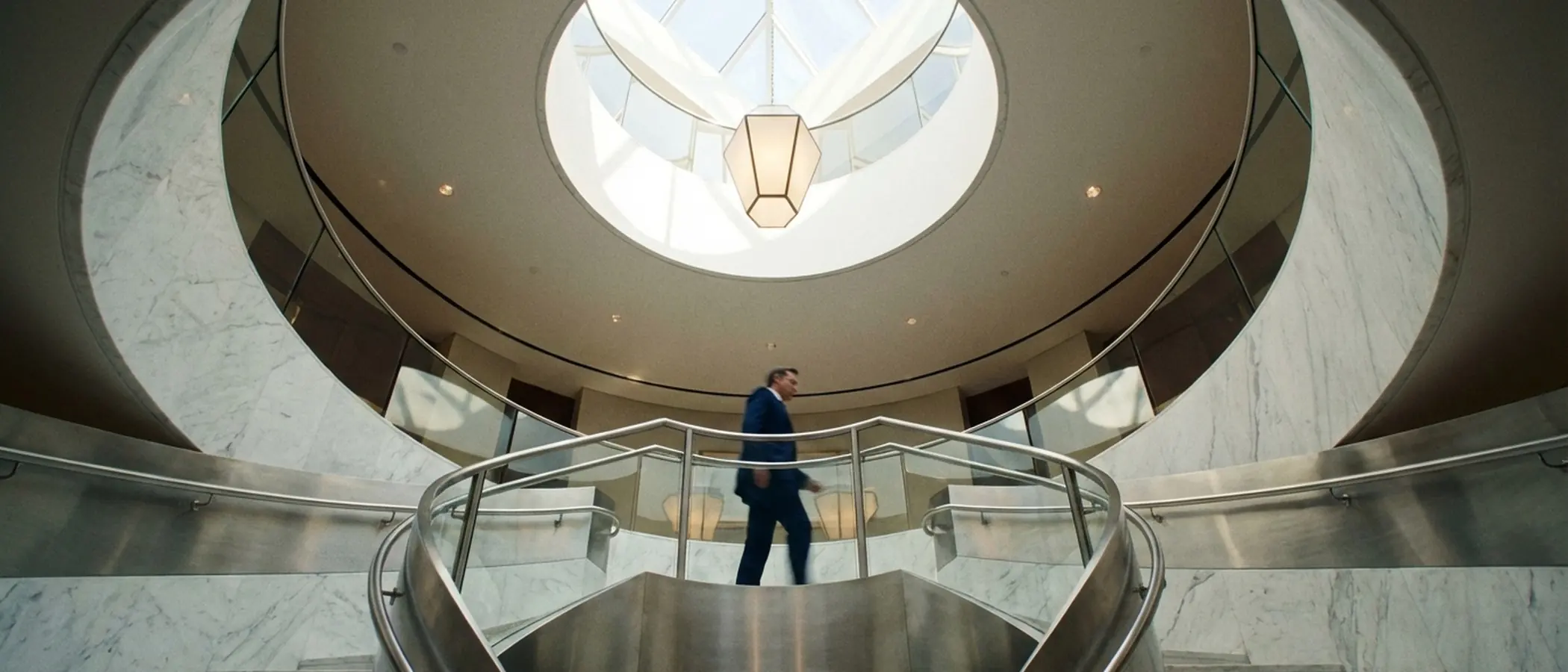 Man in suit walks up marble spiral staircase.