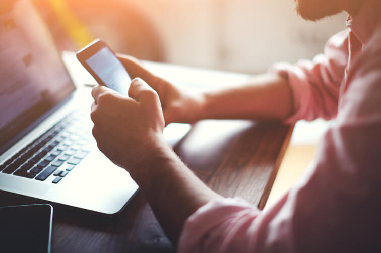 Person using smartphone while working on laptop