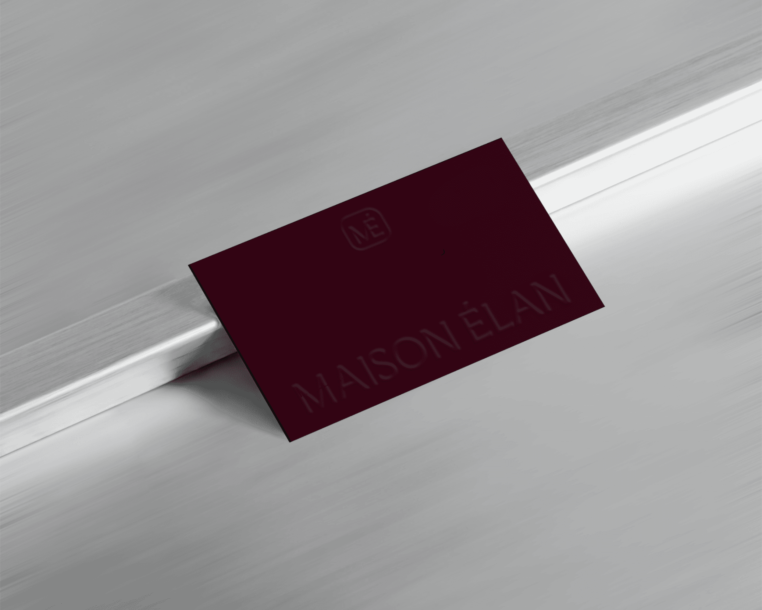 A Maison Élan business card. The card is burgandy and features the brand logo embossed on it.