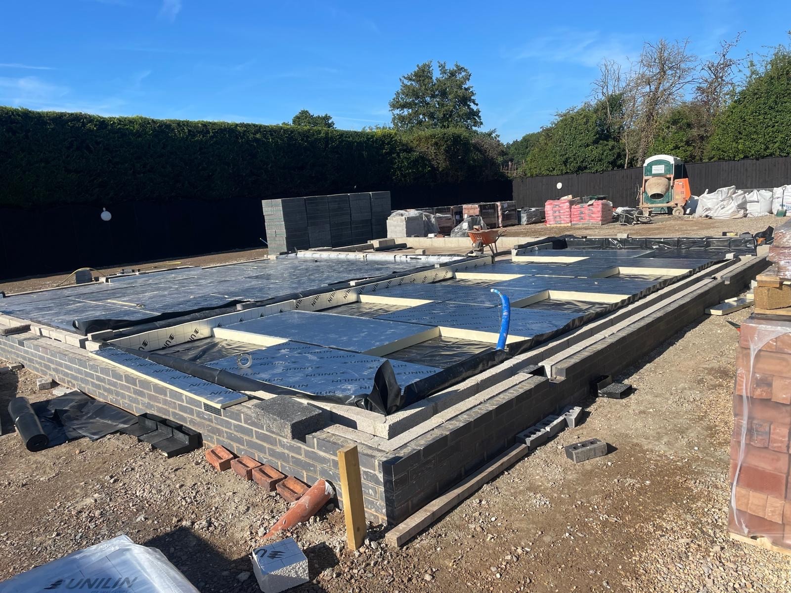 Construction site with a foundation framework and concrete slabs set against a clear blue sky.