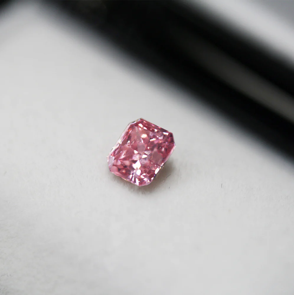Loose vivid pink diamond placed on a dark reflective surface, representing rare coloured diamond investments
