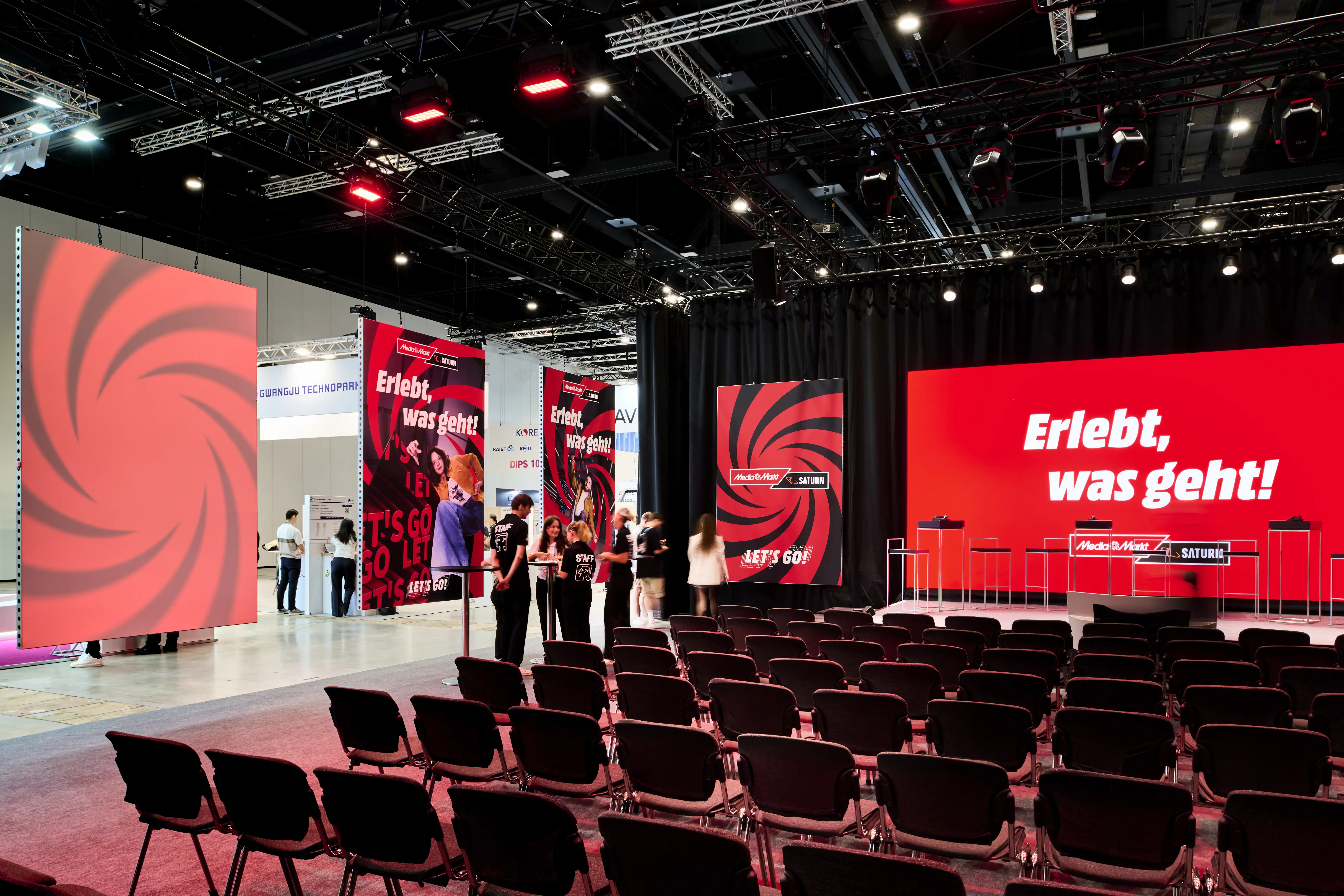 MediaMarkt Saturn presentation area at IFA with red screens, banners and rows of black chairs.