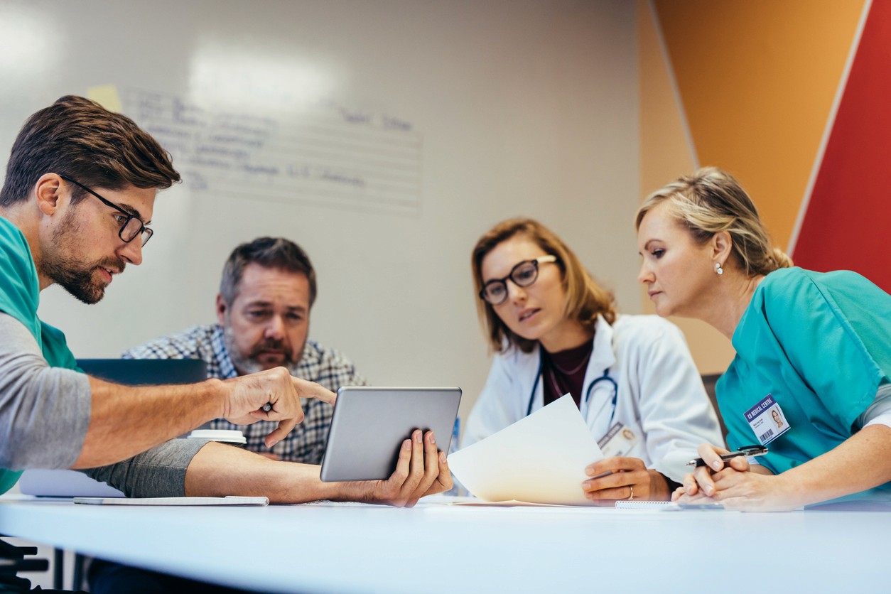 Medical team reviewing tablet and documents during a meeting. Healthcare professionals at work.