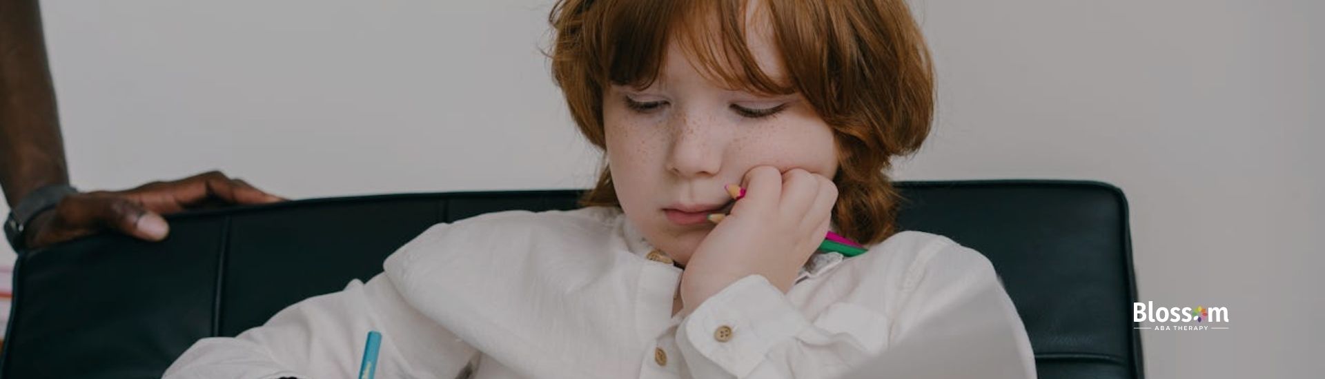 A young boy with red hair is sitting in a chair.