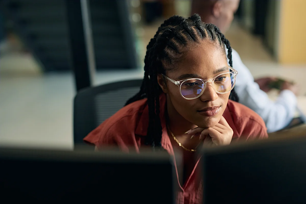 Legal professional focused on a computer screen in an open-plan office, representing careful review and analysis of legal information.