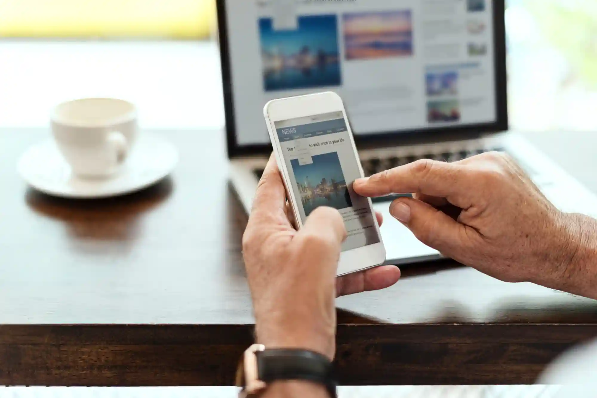 A person browses an e-commerce website on their smartphone while working at a desk with a laptop nearby.